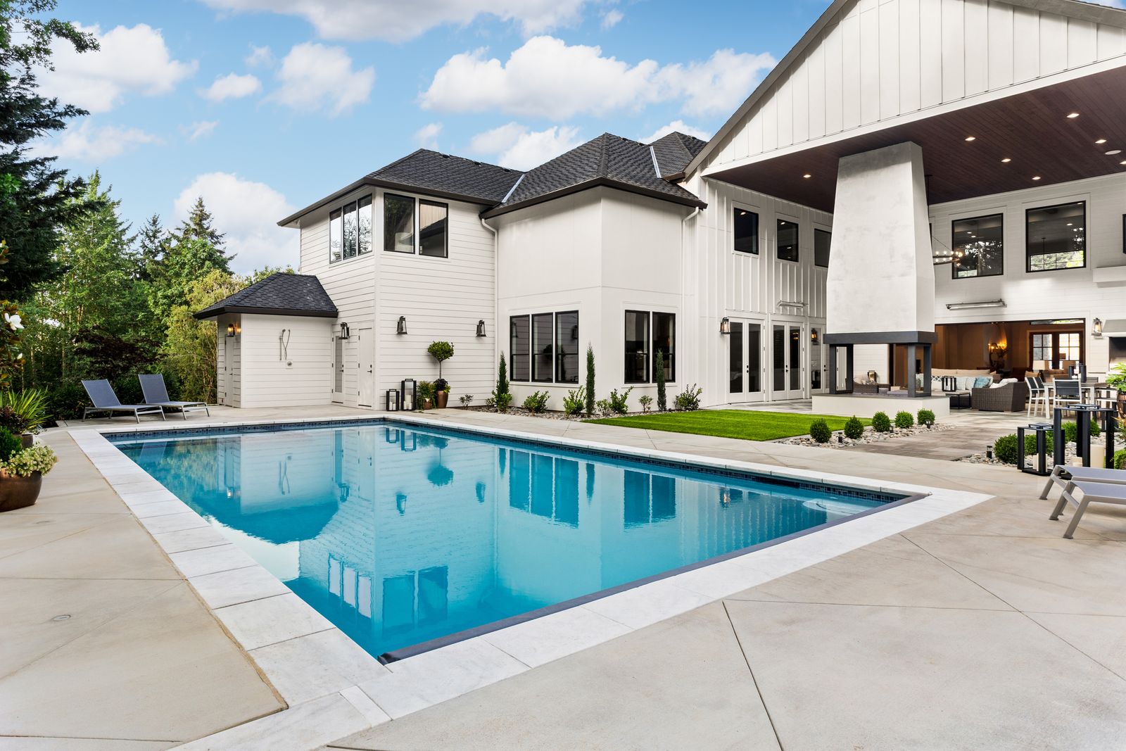 Rectangular backyard pool beside a modern farmhouse with an outdoor fireplace